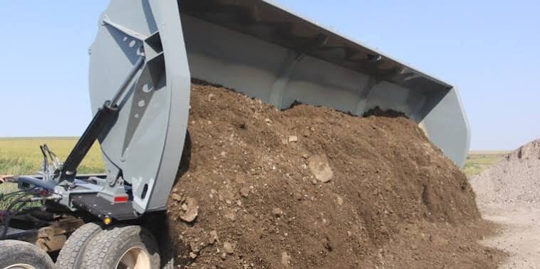 Semi side-dump trailer with tub tipped sideways and dirt pouring over the hinged dump side